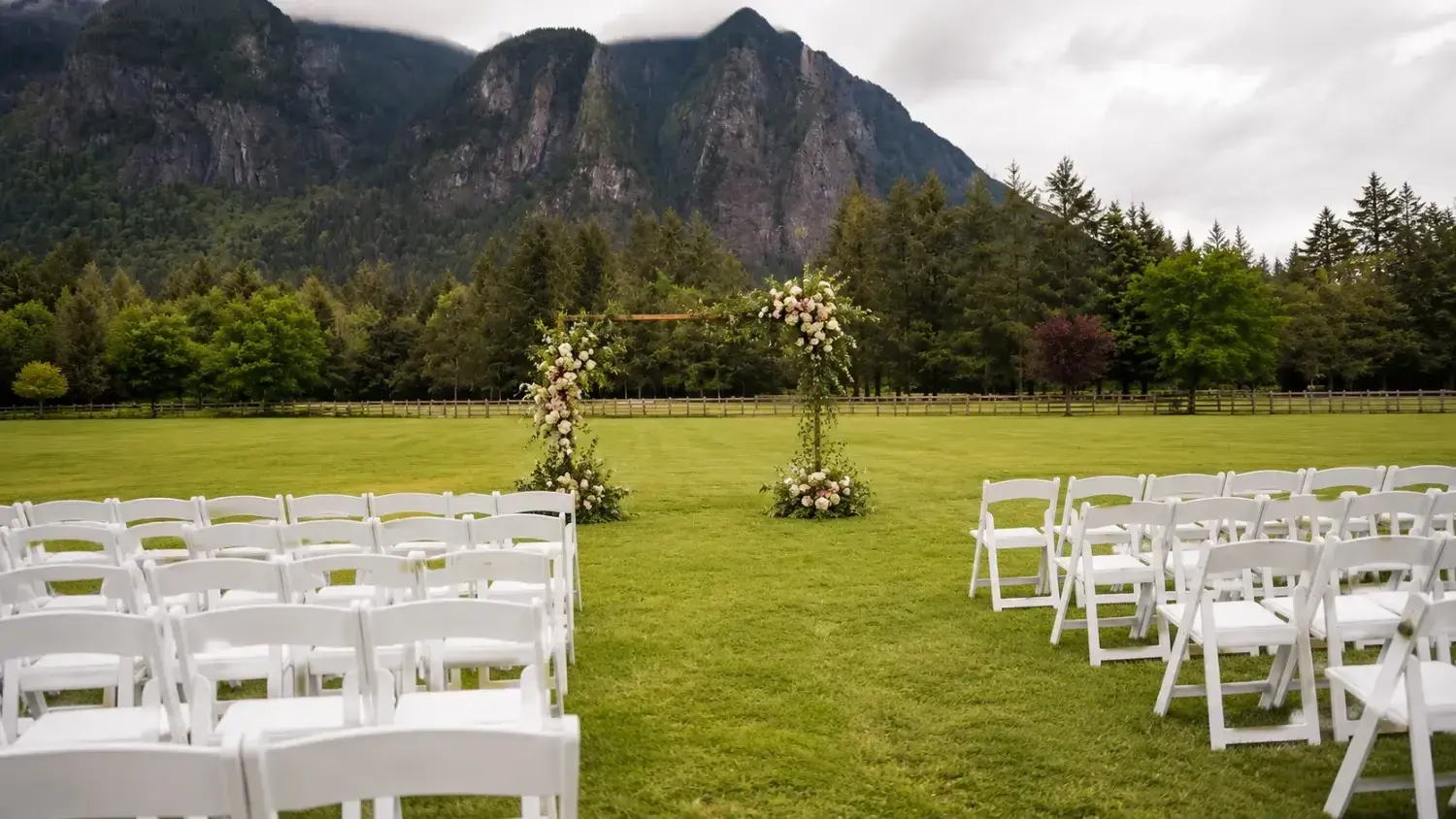 An elegant outdoor wedding ceremony setup with wooden chairs and a floral arch in a garden